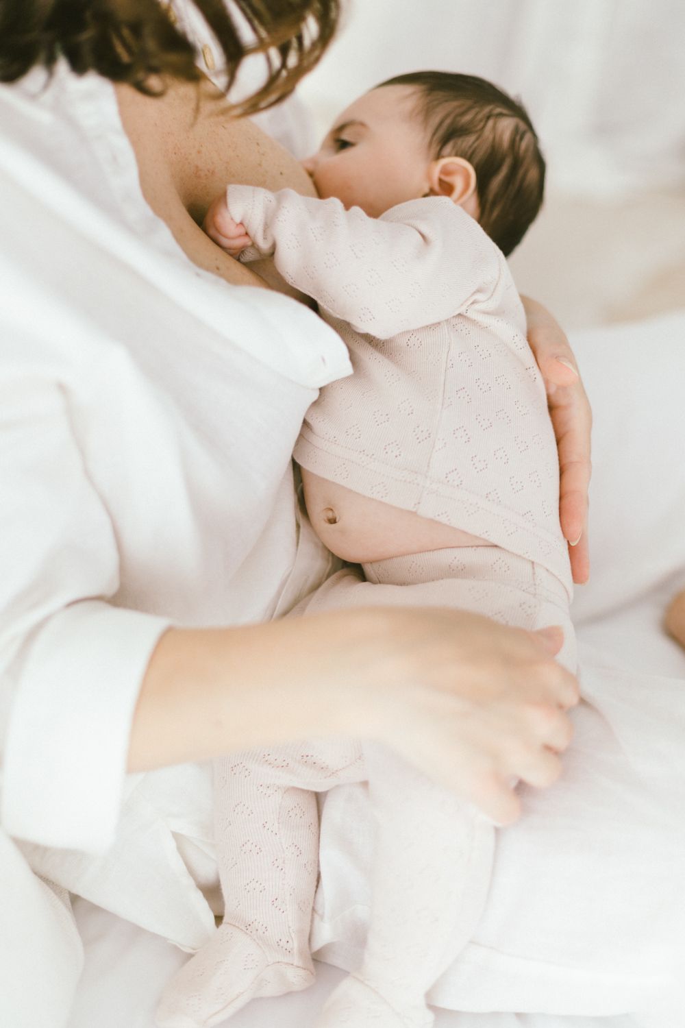 Tender nursing moment between caregiver and infant dressed in soft beige and white.