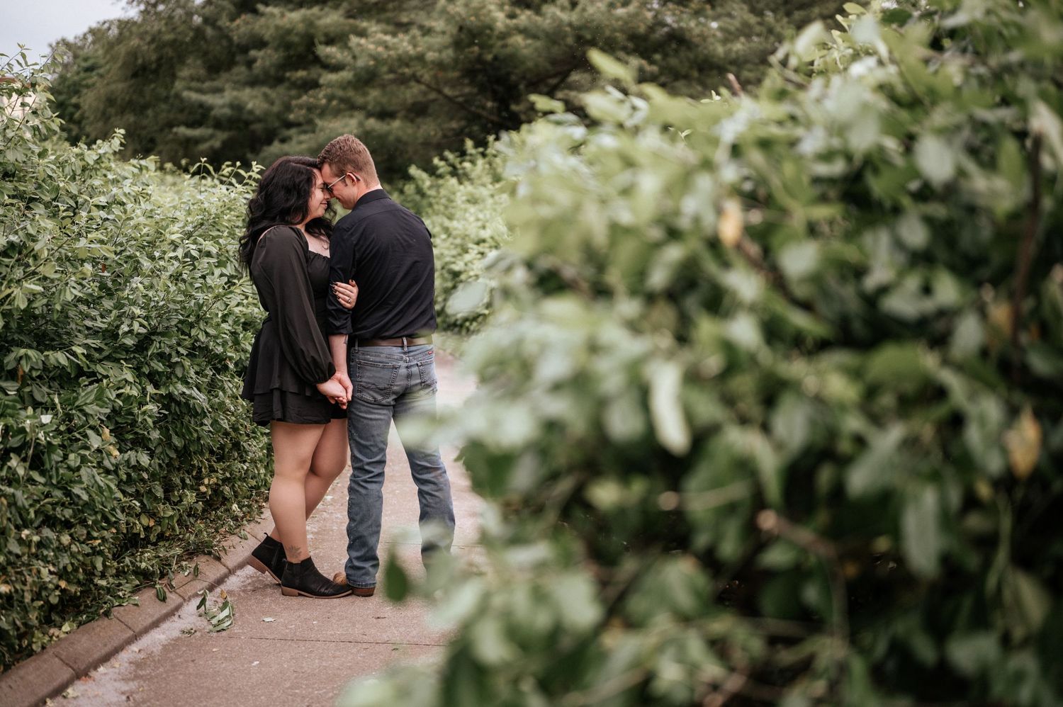 Intimate moment between couple on garden path surrounded by green foliage.