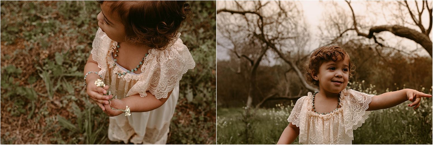 Toddler in cream-colored dress plays joyfully in nature during golden hour.