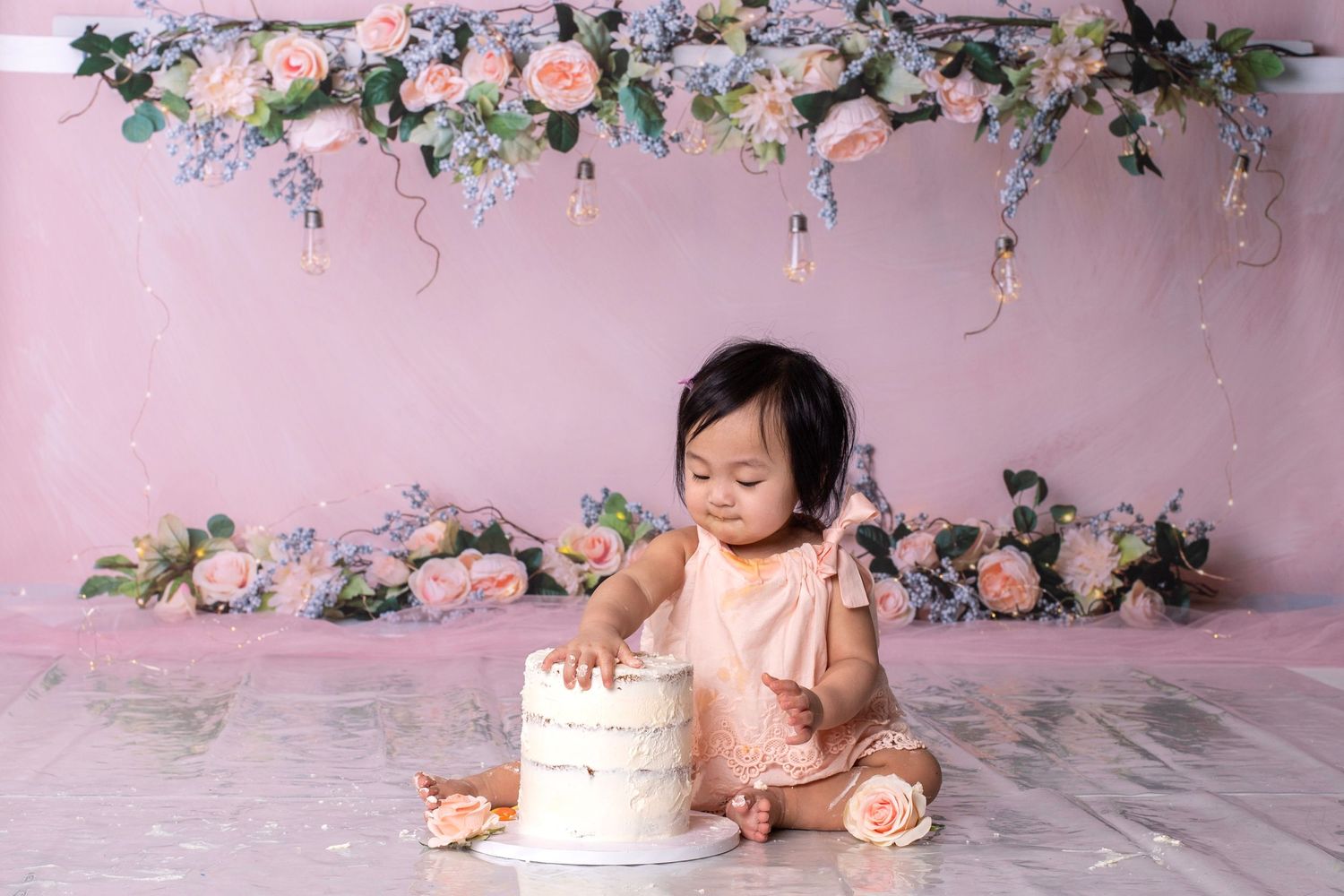 Cake smash photo session with pink floral backdrop and white birthday cake.