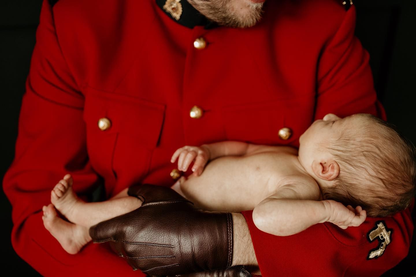 A tiny infant rests against someone wearing a bright red uniform with brass buttons.