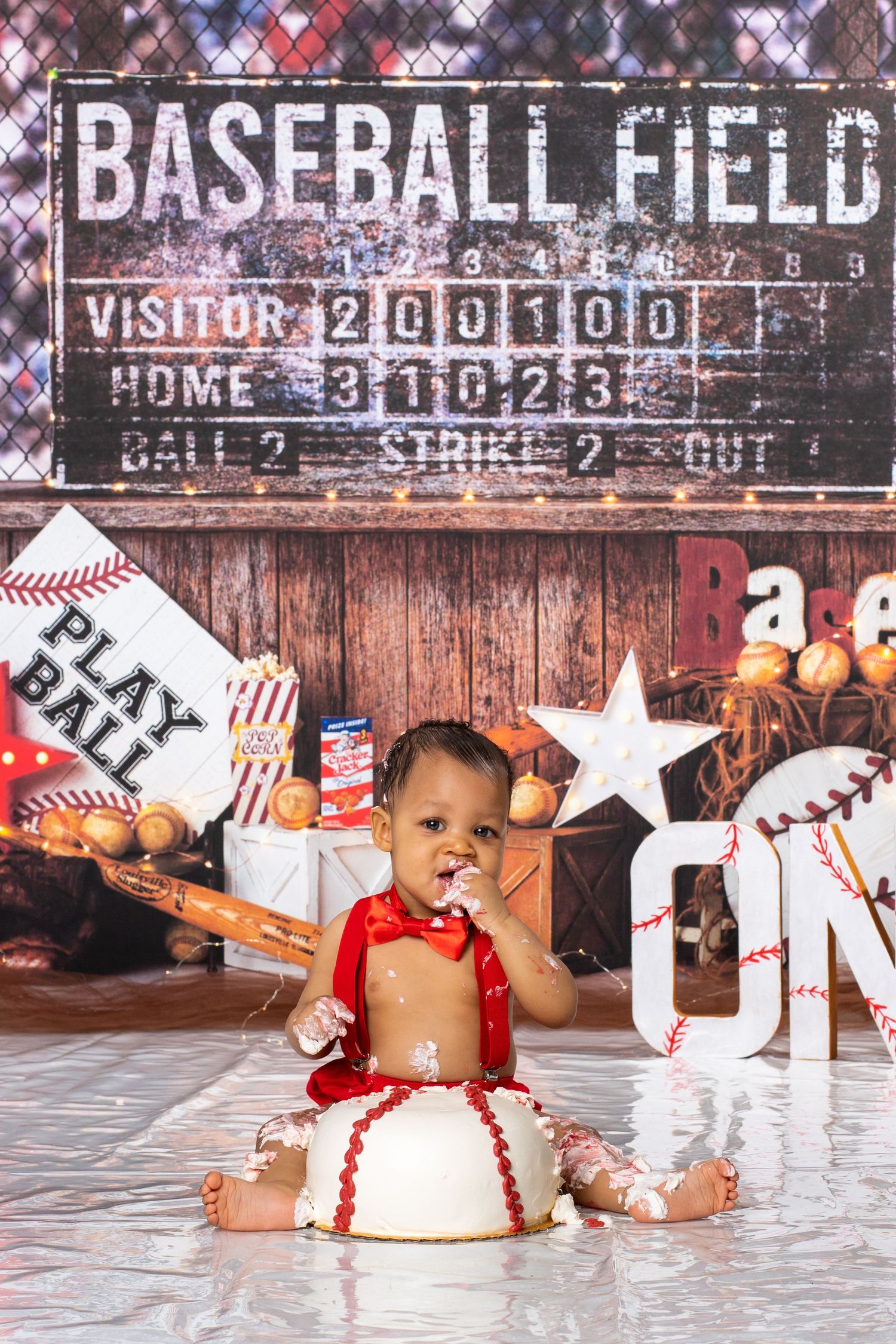 Baseball themed cake smash photo session with vintage scoreboard backdrop and sports decor.