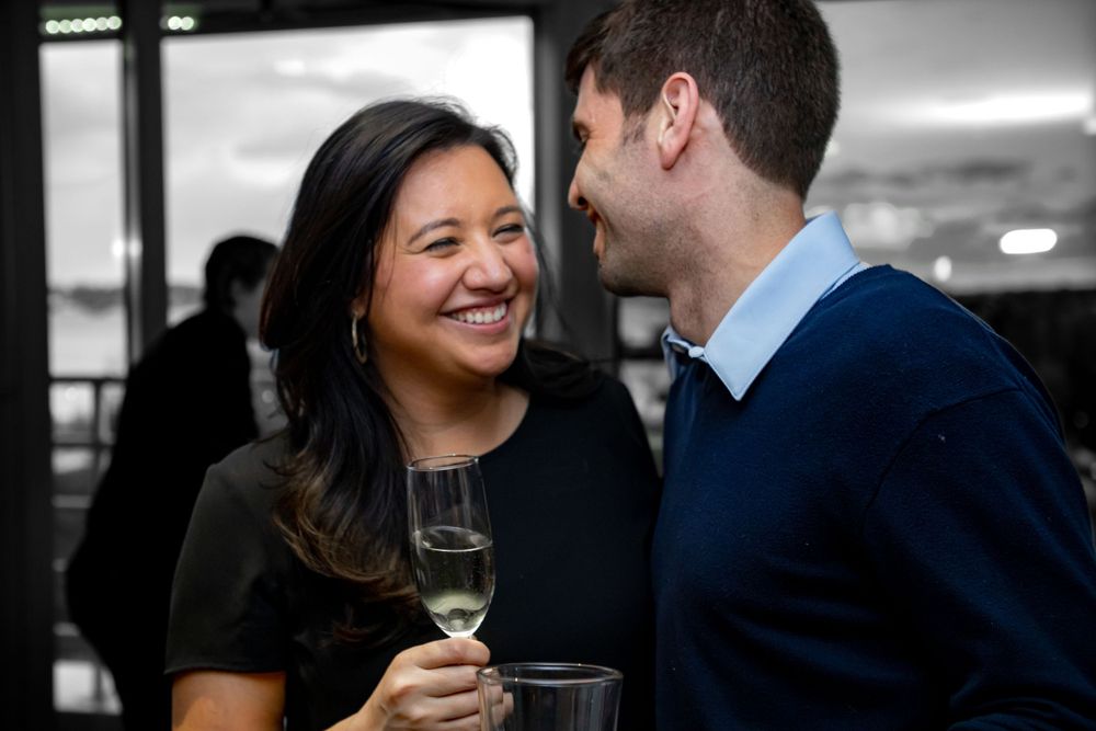 Two people share a candid moment while enjoying drinks at an indoor social gathering.