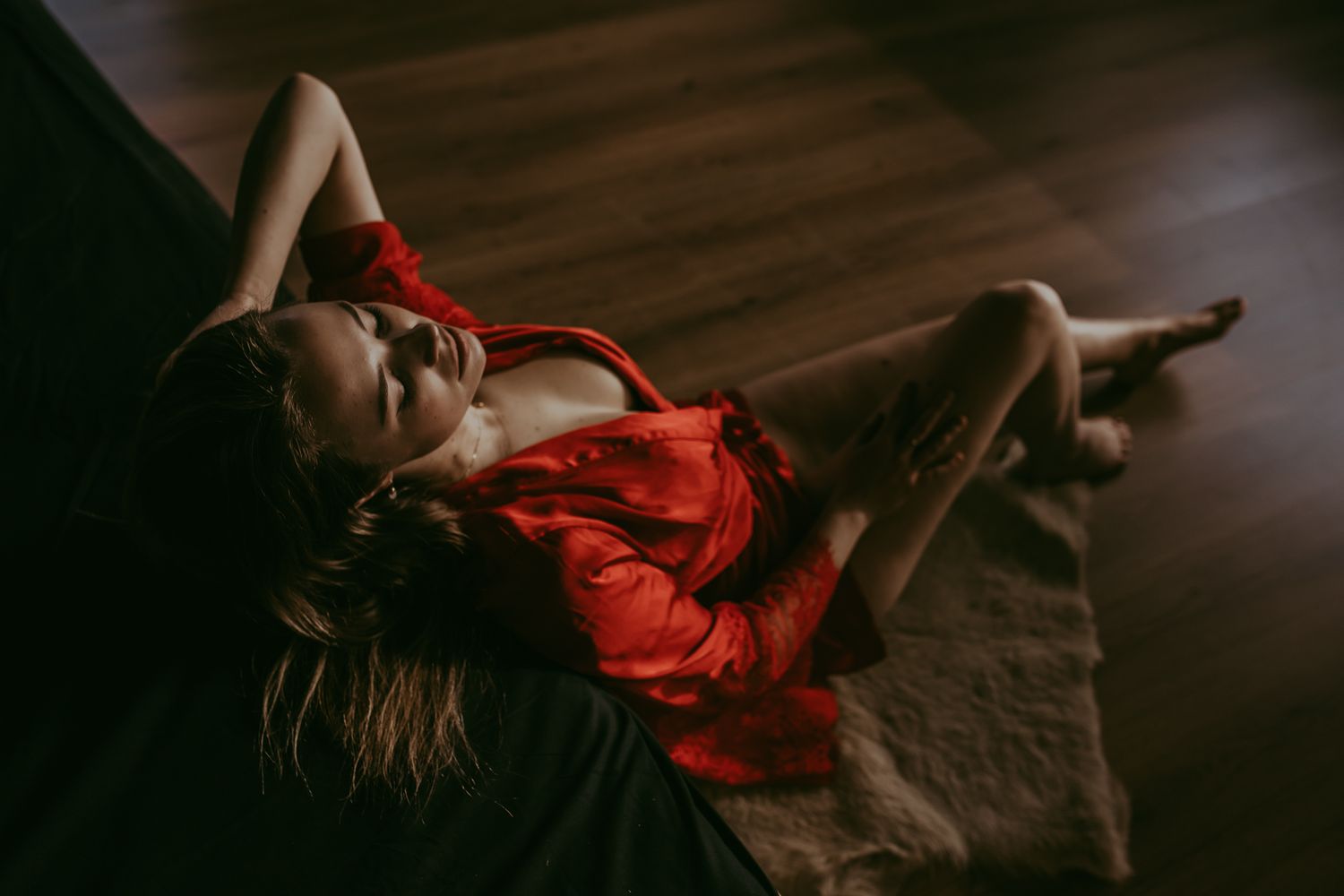 Dramatic portrait in red silk dress on dark wooden floor.