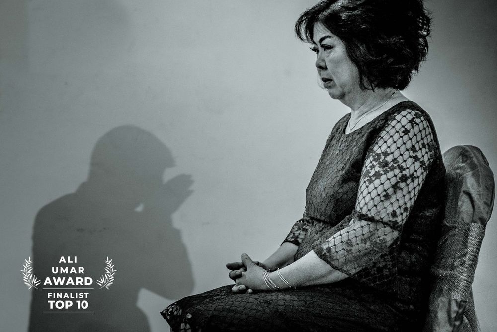 Black and white portrait of woman sitting in profile view with shadow cast on wall.