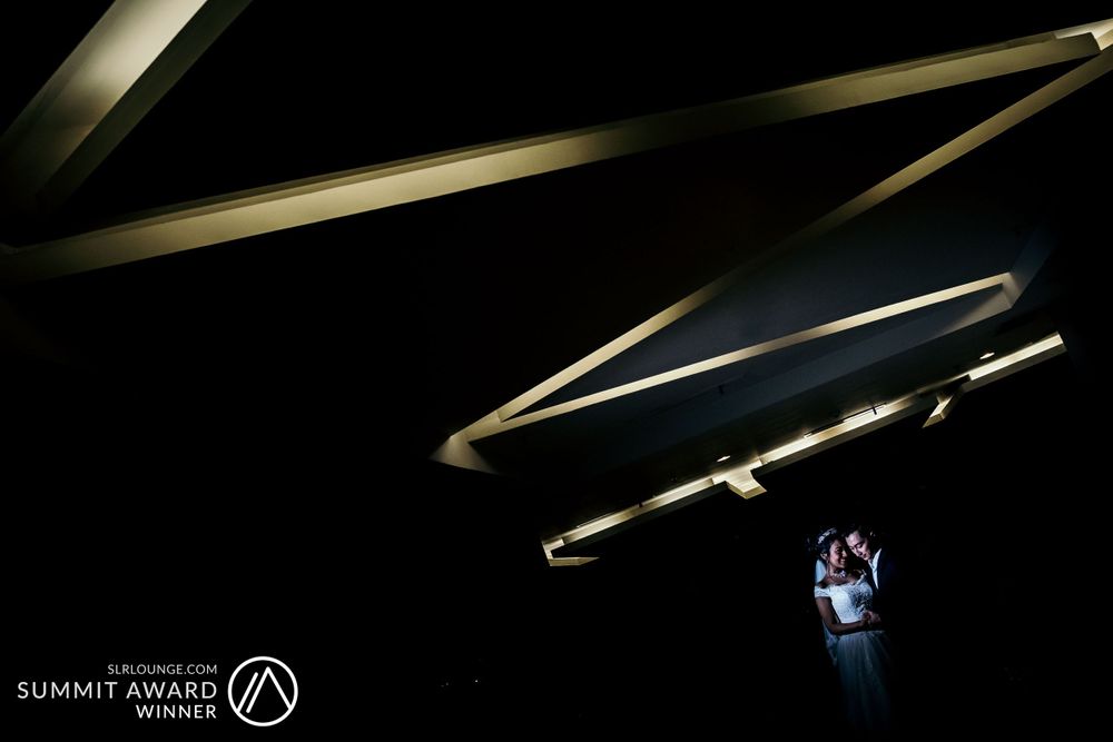 Artistic wedding photo with geometric lighting patterns and a small illuminated figure below.