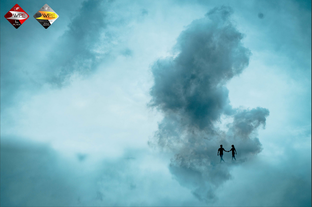 Silhouetted couple standing beneath dramatic stormy clouds in turquoise sky.