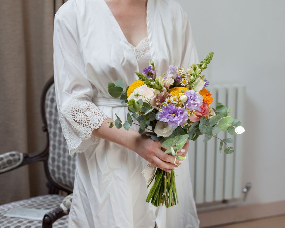 Une future mariée en peignoir en dentelles tient un beau bouquet de fleurs colorées