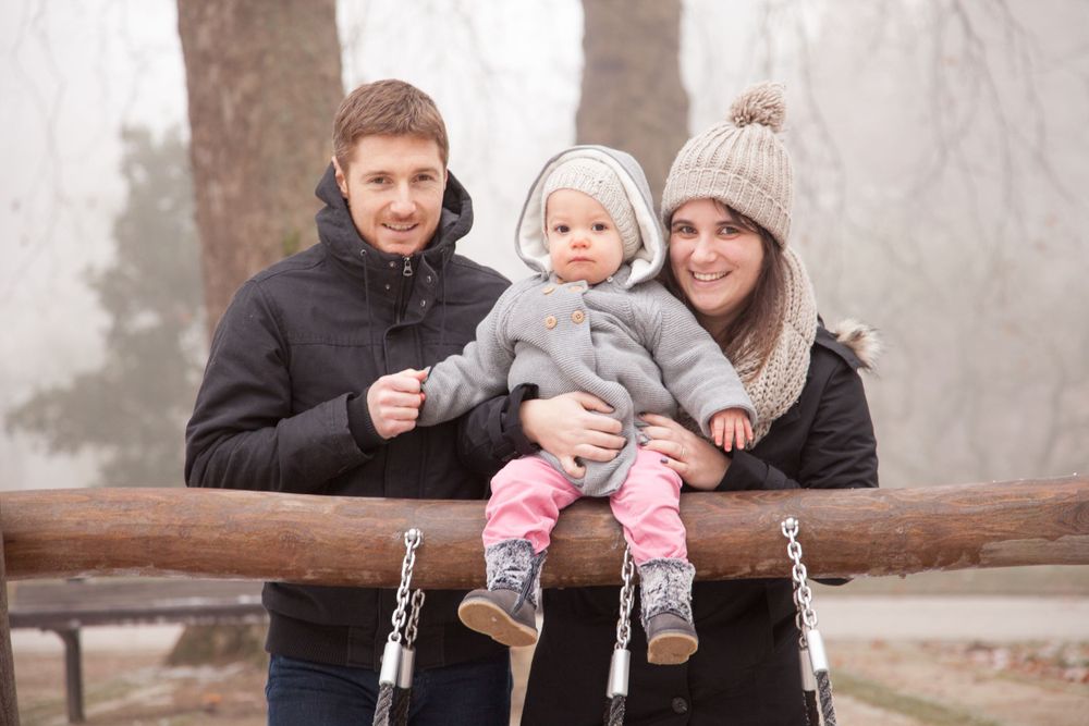 Portrait de famille en hiver, un coupe et son bébé sont habillés chaudement et sourient au photographe.
