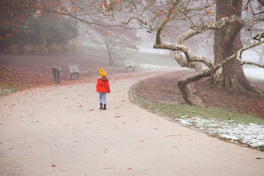 Photo d'une jeune fille habillée en rouge dans un parc. L'ambiance est hivernale, il y a du brouillard et de la neige.