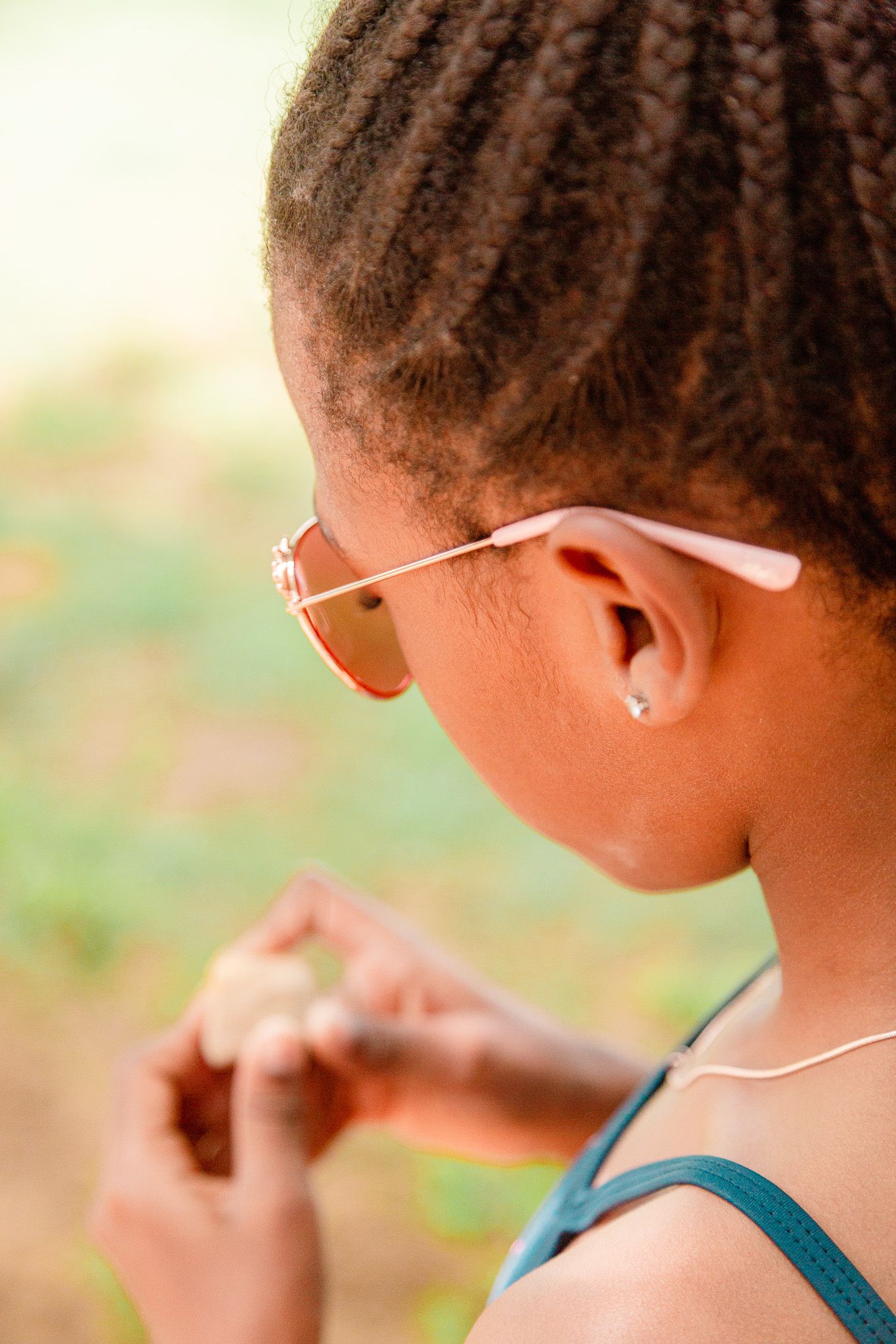 Looking over the shoulder of a young girl wearing sunglasses who is looking at a rock