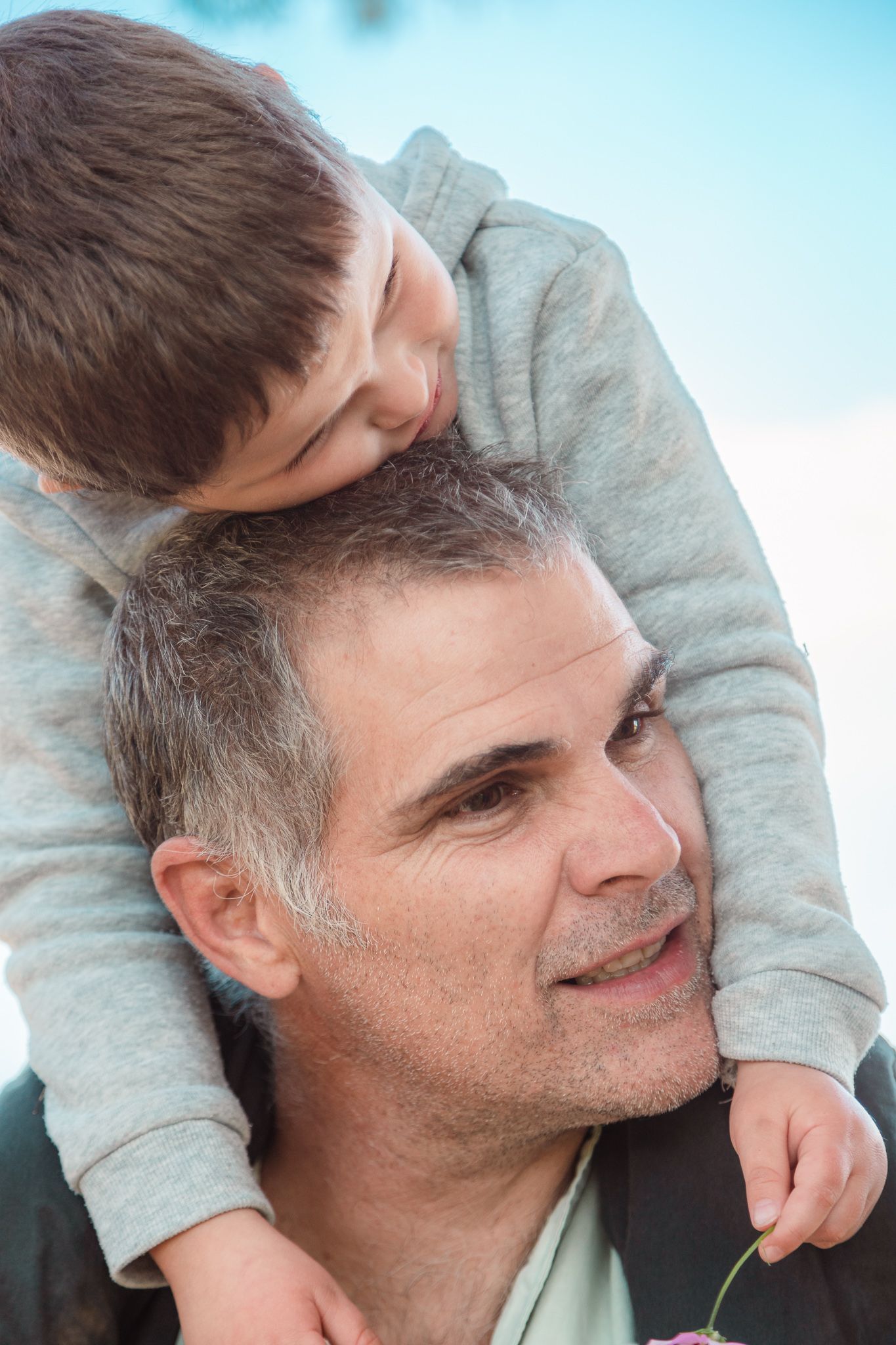 Young boy being carried on his dad's shoulders and he's resting his head on his dad's head