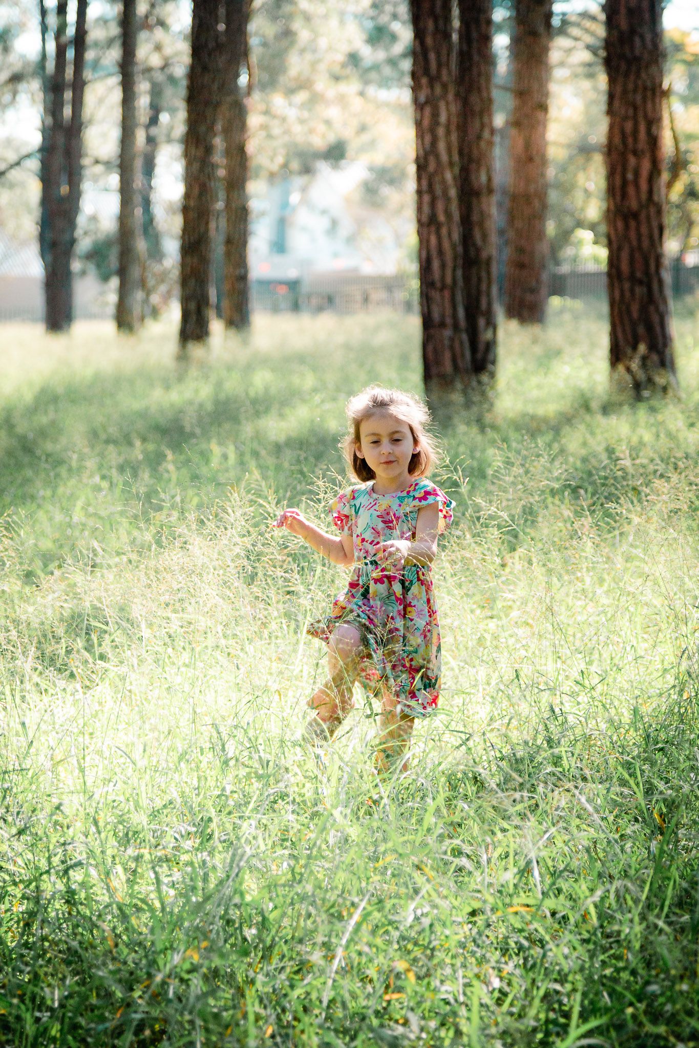Young child running through the tall green grass in a forest with sunlight shining through