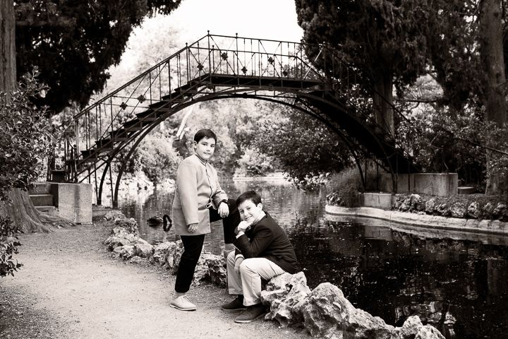 Black and white photo of couple sitting on stone bridge in romantic garden setting.