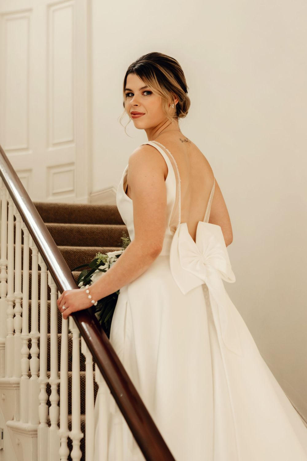 Wedding dress with elegant bow back detail shown on carpeted staircase with white railings.