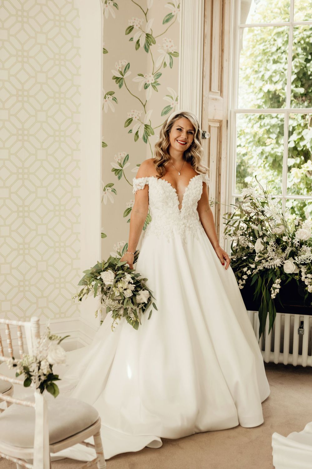 Wedding gown with off-shoulder lace bodice and full skirt captured in elegant room with floral accents.