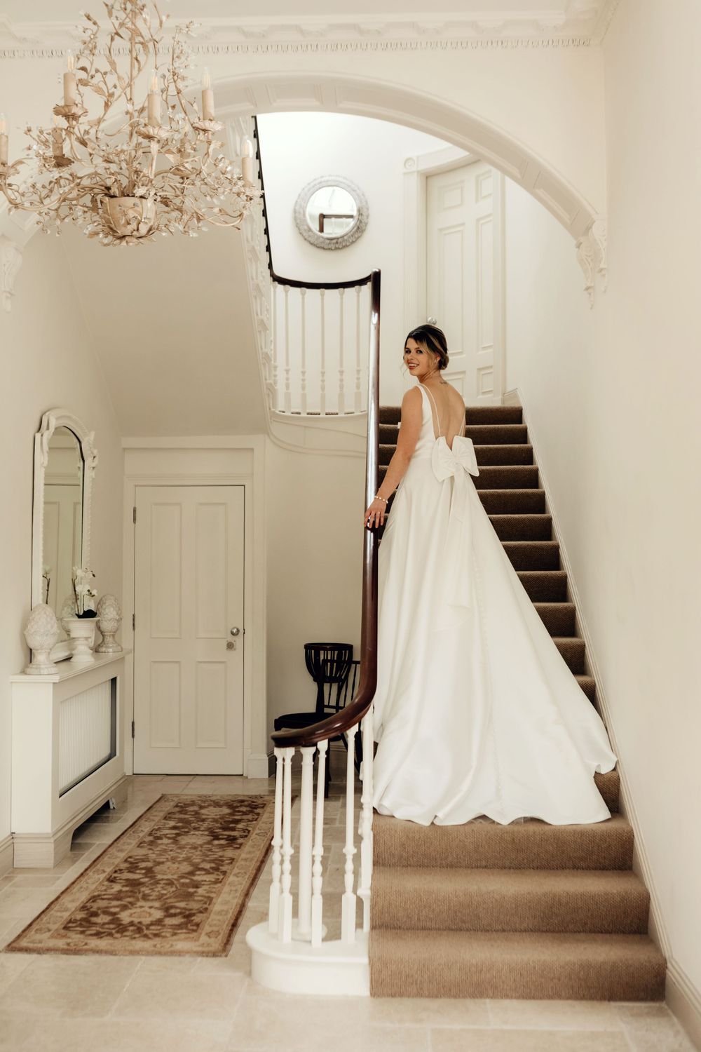 Back view of wedding gown with bow detail on classic staircase under crystal chandelier.