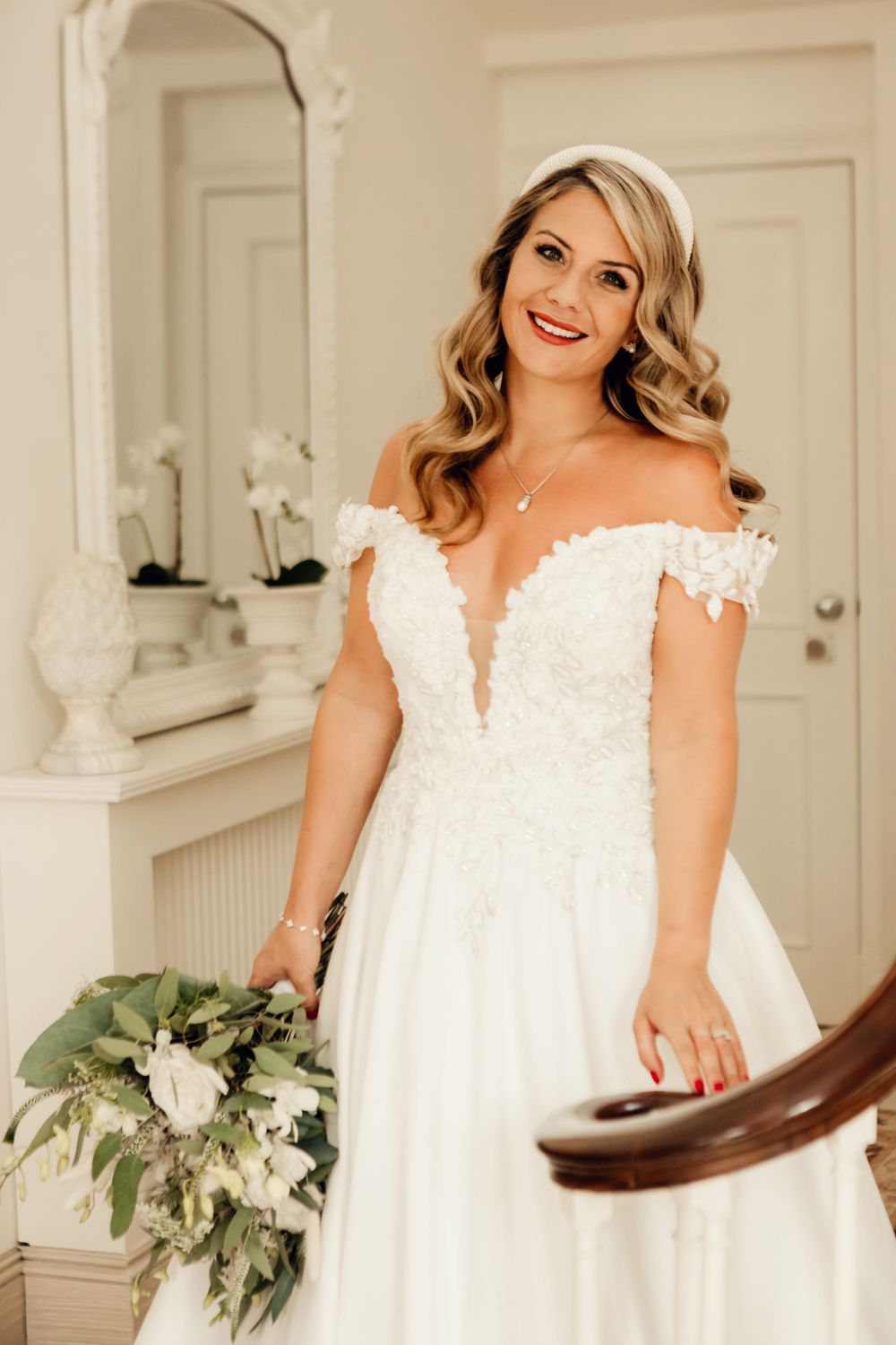 Off-shoulder wedding dress with plunging neckline and lace details captured by ornate mirror.