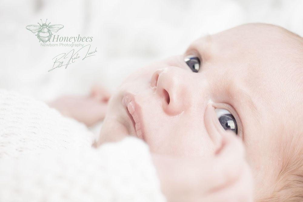 baby laying on his back in white baby grown with white fluffy background and blue eyes