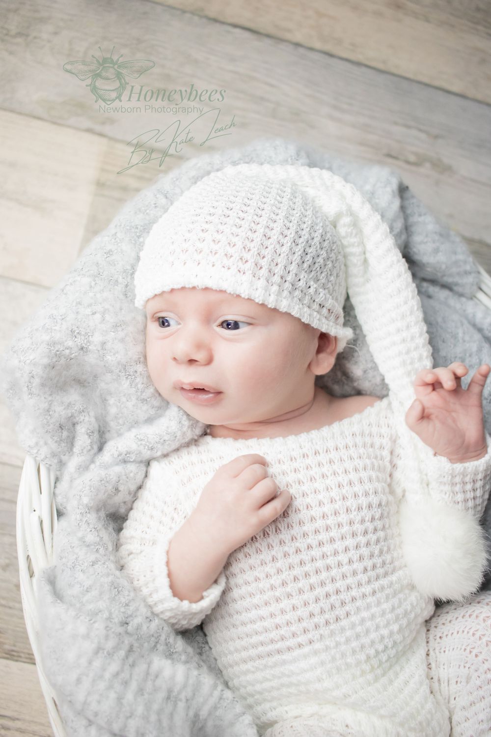 newborn photos shoot with baby in white baby grown and sleep hat in a white basket lined with grey blanket