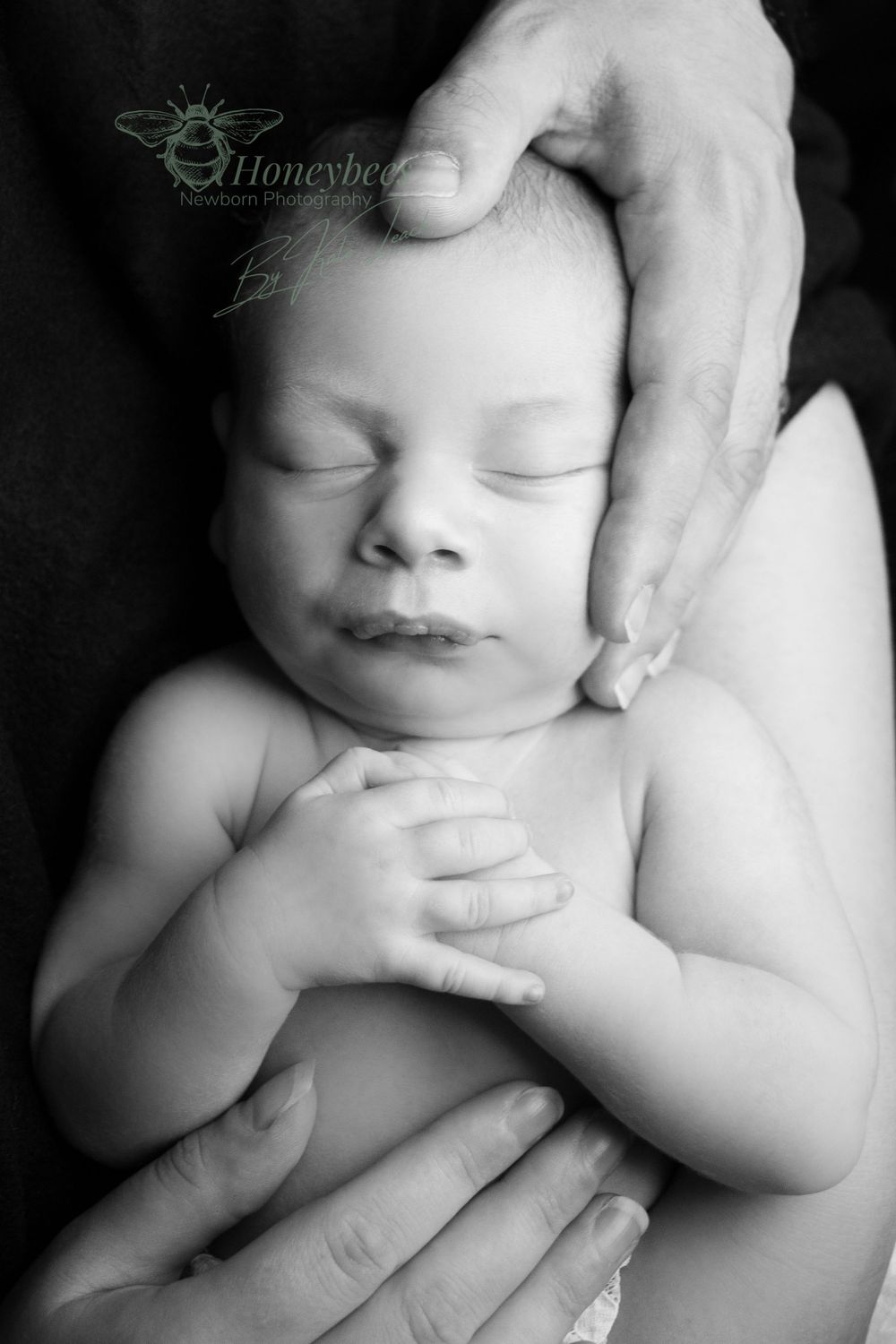 black and white baby sleeping with hands on his check and dads hand holding his head and mums hand resting on his tummy