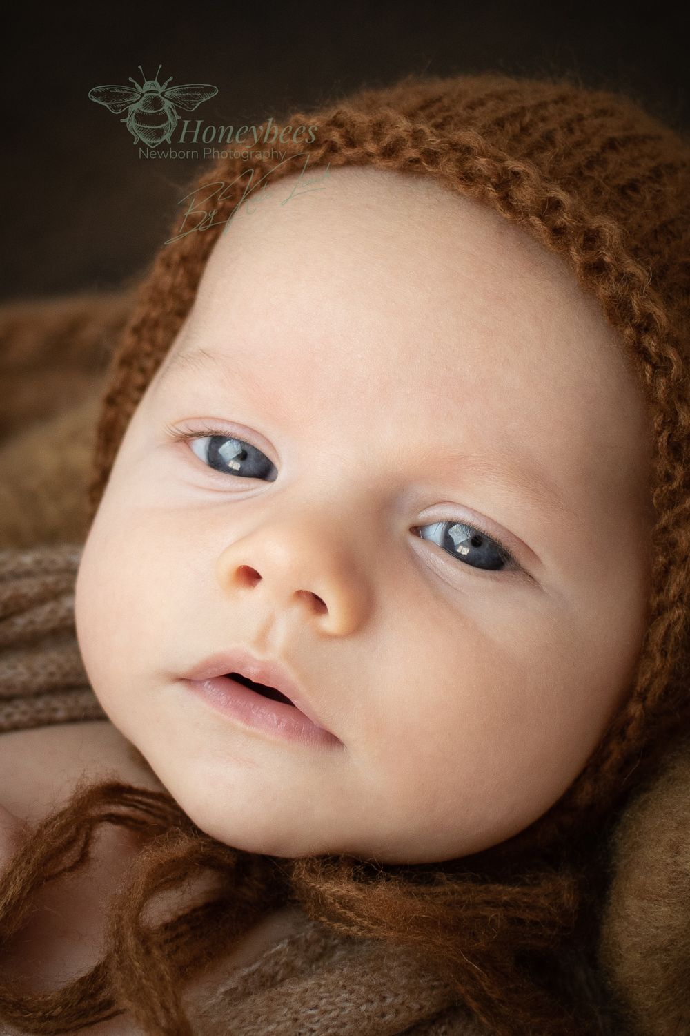 bay looking sleepy in brown knitted Bonet for newborn baby photo shoot with warn natural tones