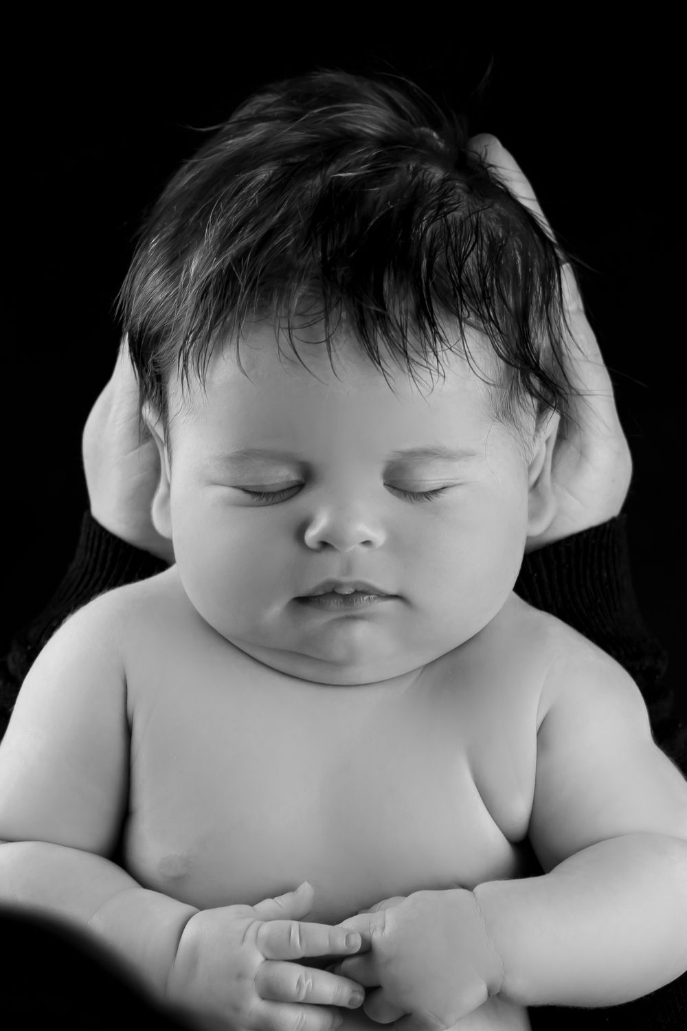 newborn photoshoot of baby asleep held by mothers hand in black and white