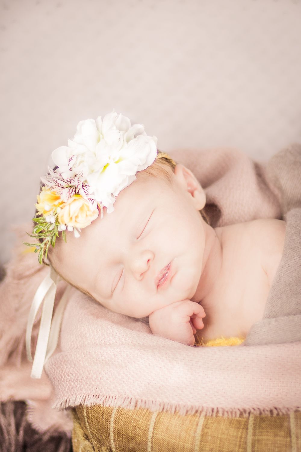 newborn photo shoot of baby in a bucket sleeping pink flowers in her hair