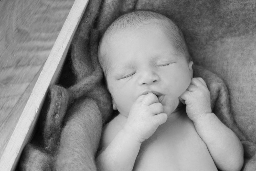 Baby asleep in a wooden box with hand in mouth black and white