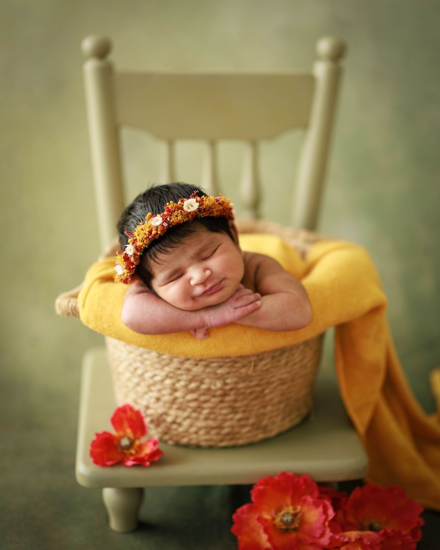 Newborn photography featuring baby sleeping in basket on vintage chair with orange flowers.