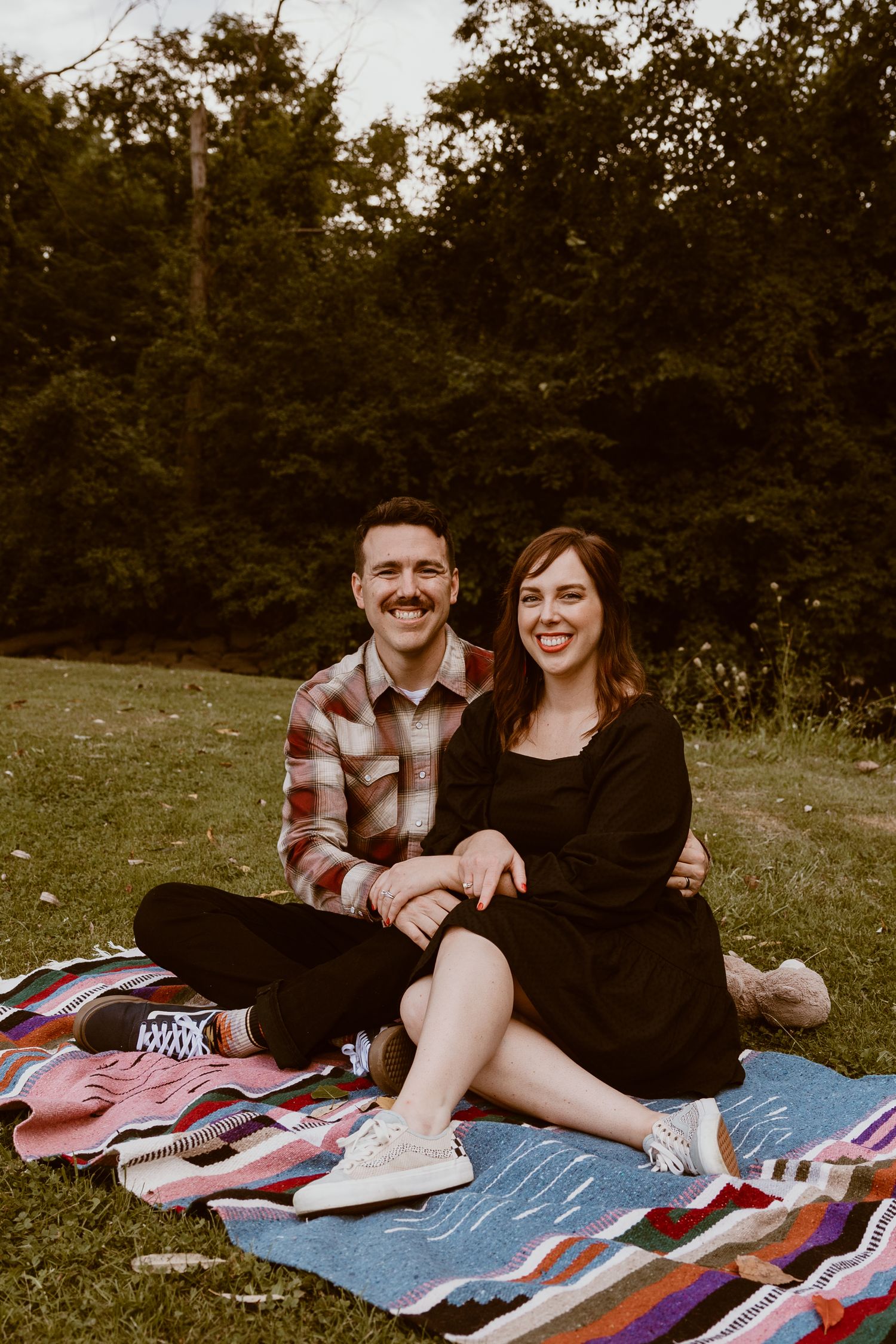 Couple sitting on a blanket enjoying a picnic in a park setting.