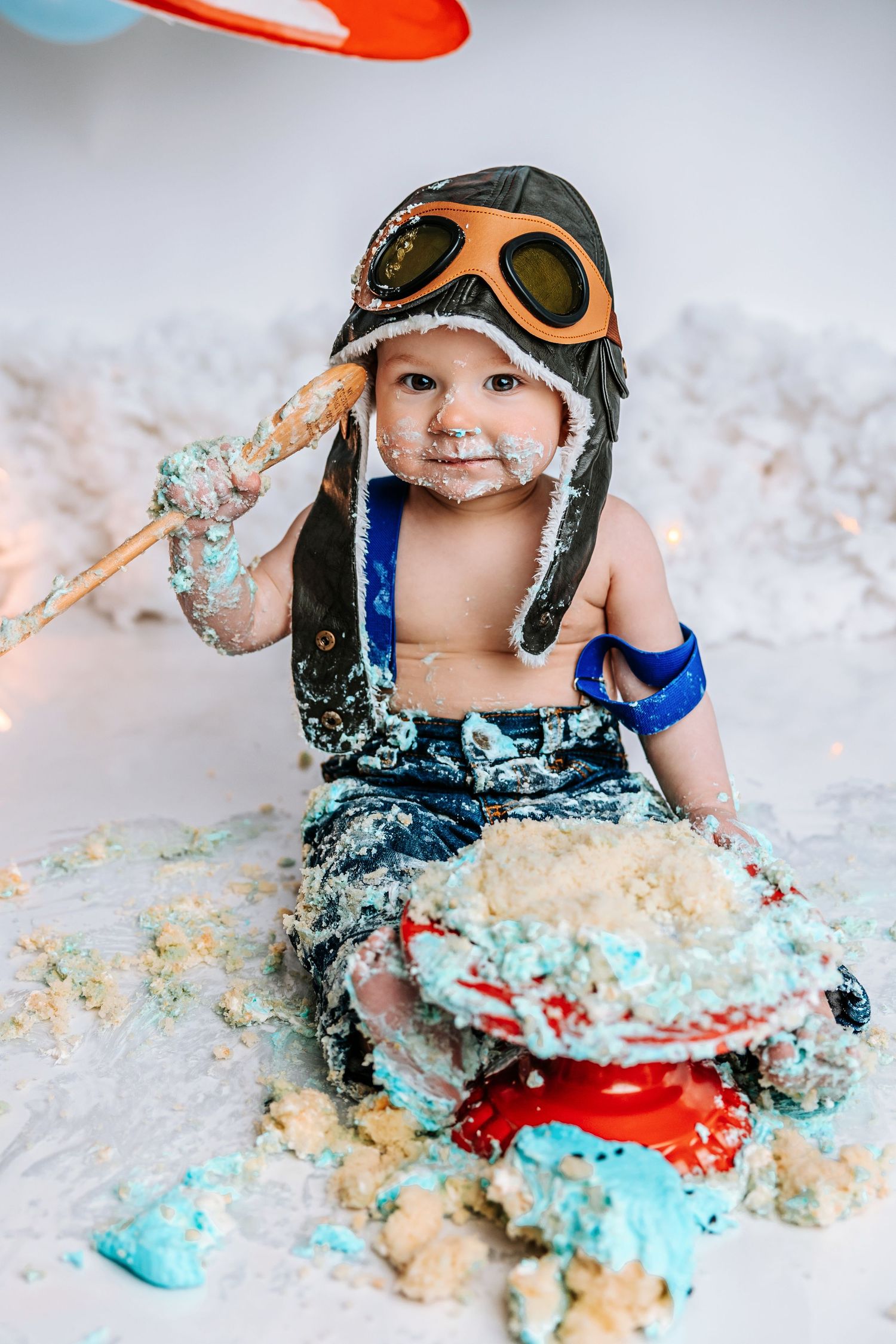 Baby in vintage aviator costume playing in colorful cake smash photography session.