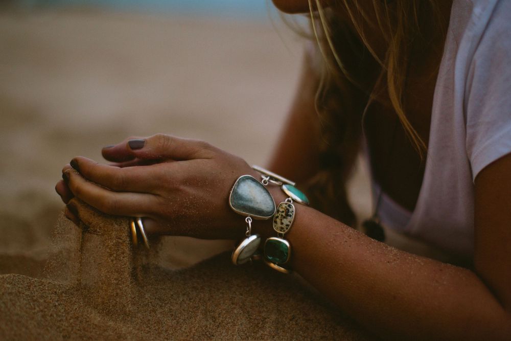 Hand with turquoise bracelet and rings resting on sandy surface in warm lighting.