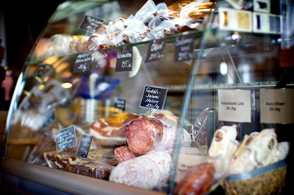 Close-up of deli display case showing various meats and prepared foods behind glass.