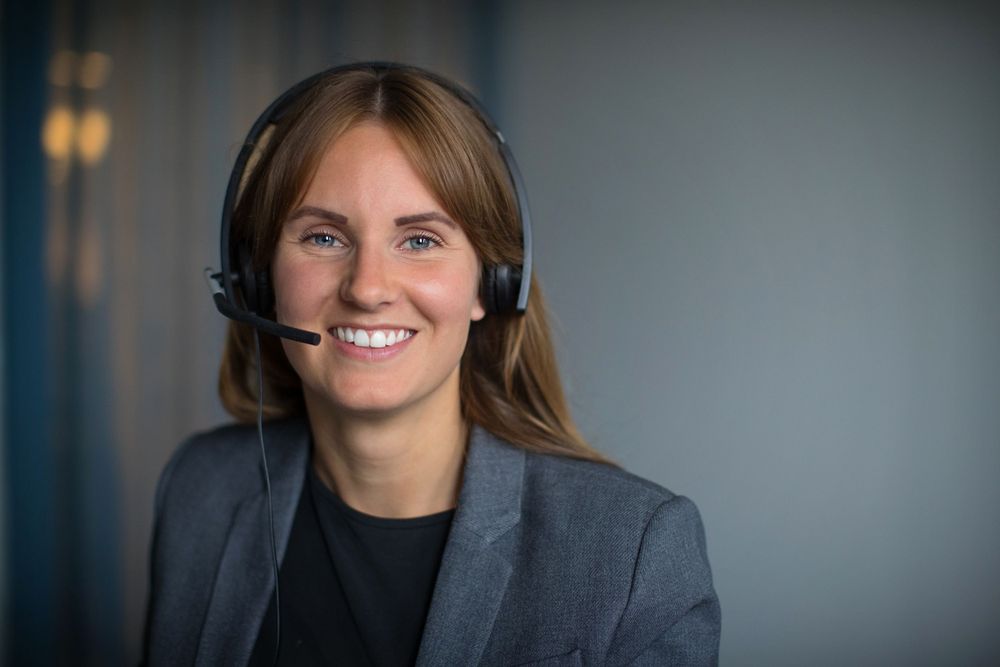 Professional wearing headset and business attire against grey background.