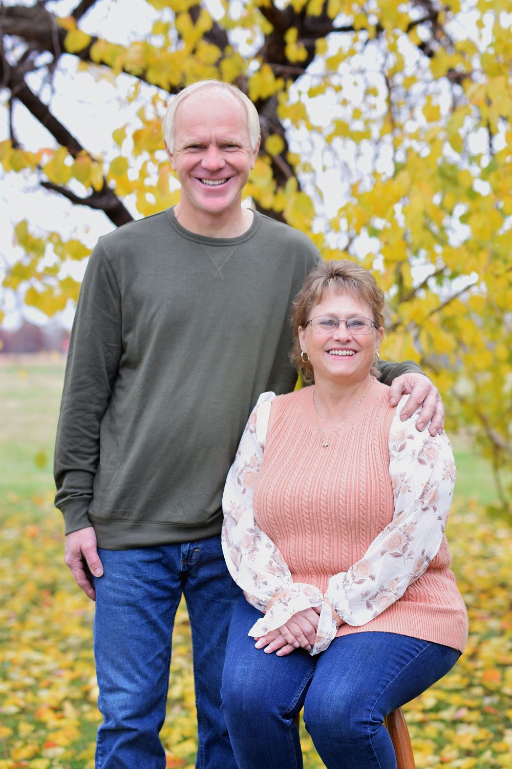 Couple in casual autumn clothing sitting together under yellow fall foliage.