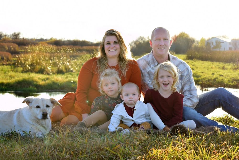 Family with white dog sitting together in field during golden hour sunset.