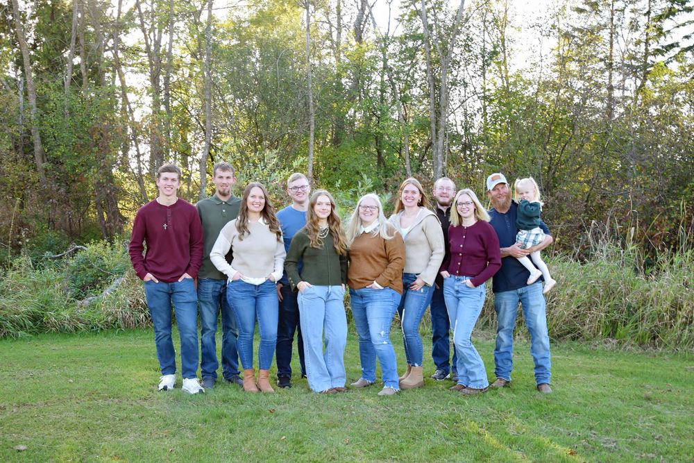 Large family group in casual attire standing together outdoors with autumn foliage background.