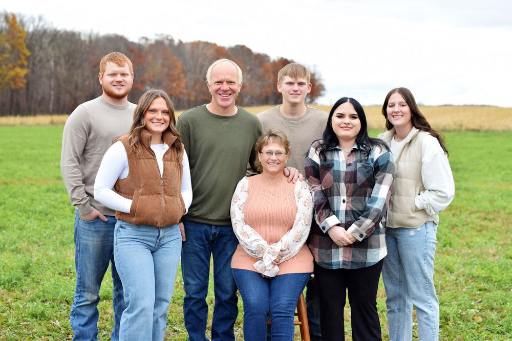 Multi-generational family group portrait in casual attire standing in autumn field.