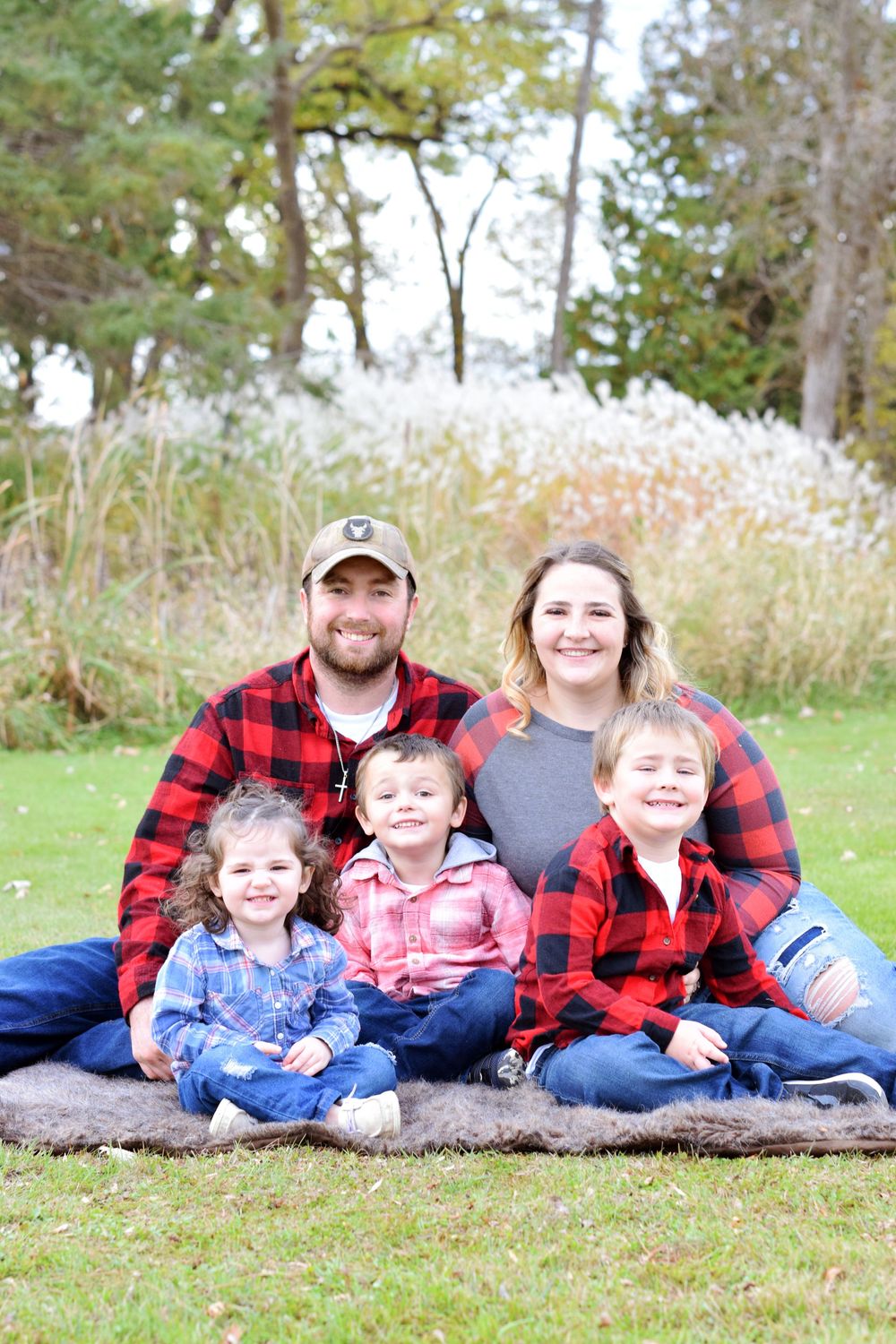 Family wearing coordinating plaid shirts sitting together on blanket outdoors in fall.