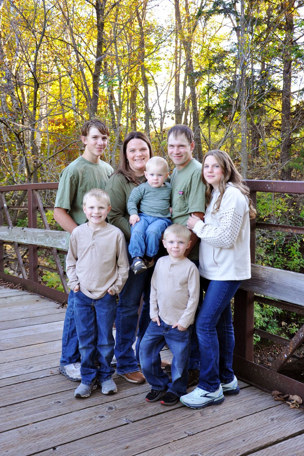 Family group portrait on wooden deck surrounded by autumn trees with yellow leaves.