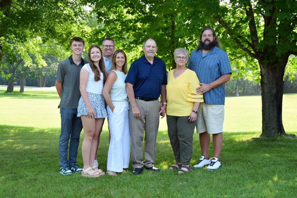 Group portrait of family members standing together on grass under shade trees in summer.