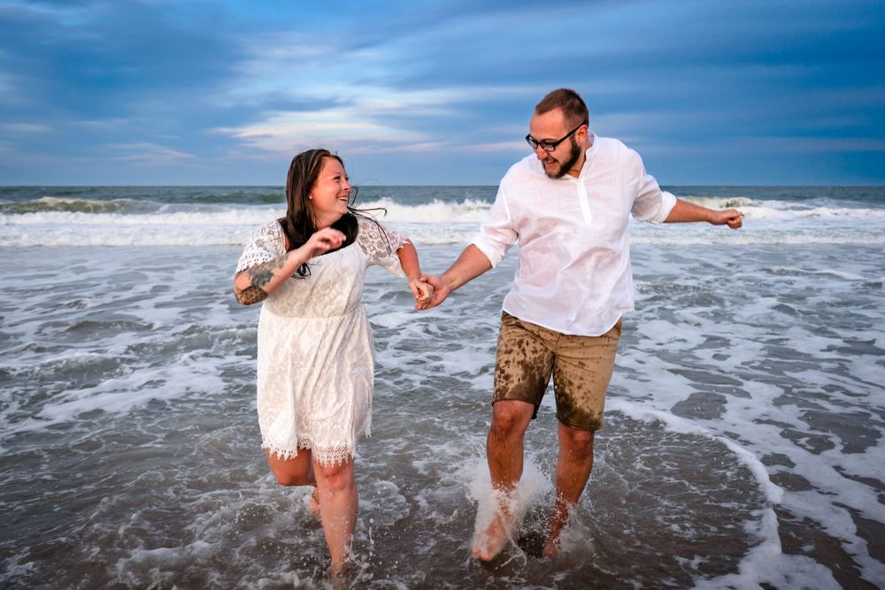 Couple splashing and playing in ocean waves during a beach photoshoot.