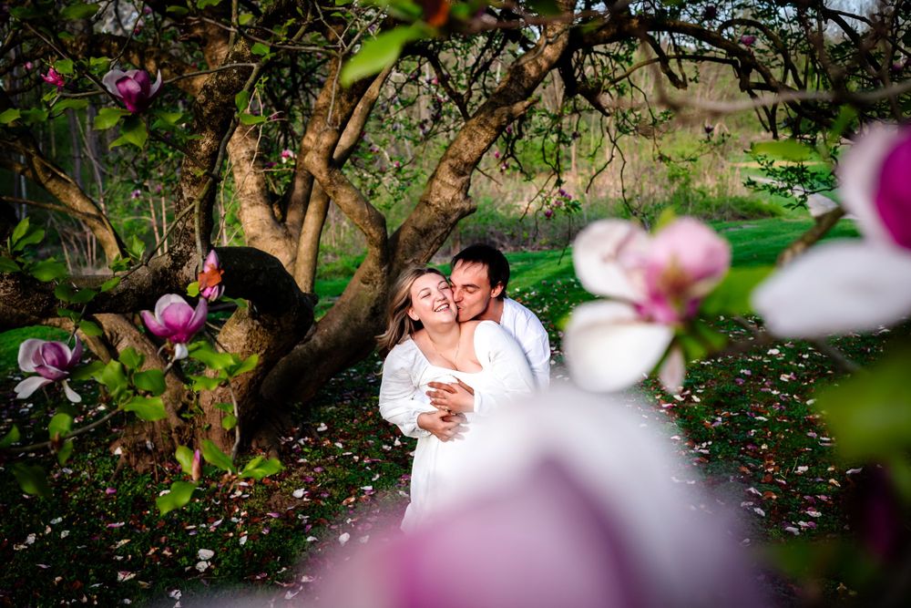 Wedding couple photographed through blooming cherry blossoms in a garden setting.