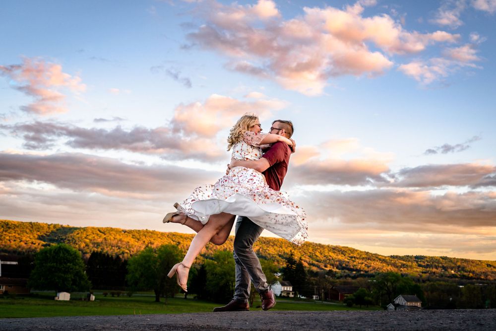Couple dancing in a golden field during sunset with dramatic sky.