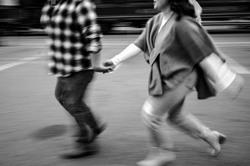 Motion blurred black and white photo of two people walking quickly past each other on a street.