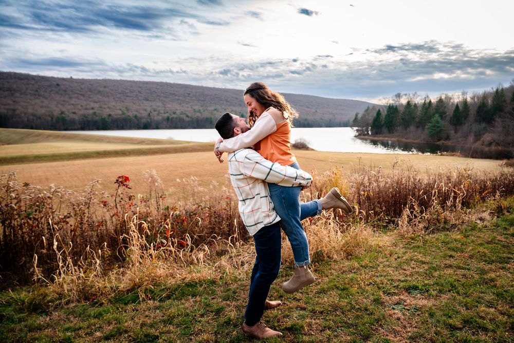 A couple dances together in a golden wheat field at sunset with mountains in the background.
