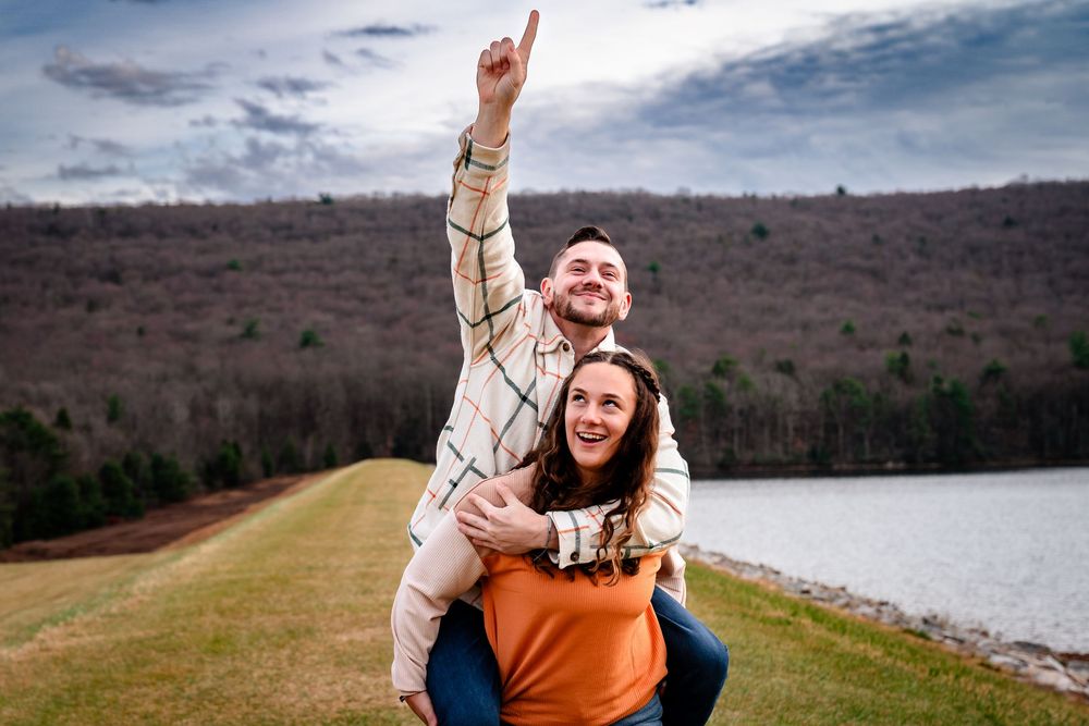 Two people having fun outdoors with piggyback ride by a lake and mountains on a cloudy day.