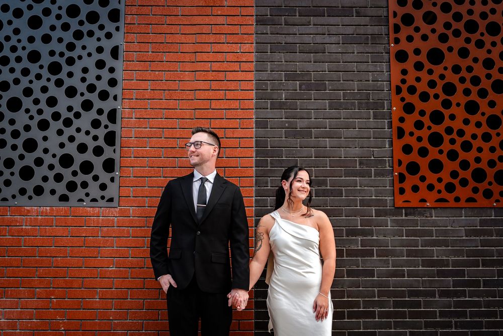 Wedding couple poses against modern brick wall with decorative circular patterns in orange and black.