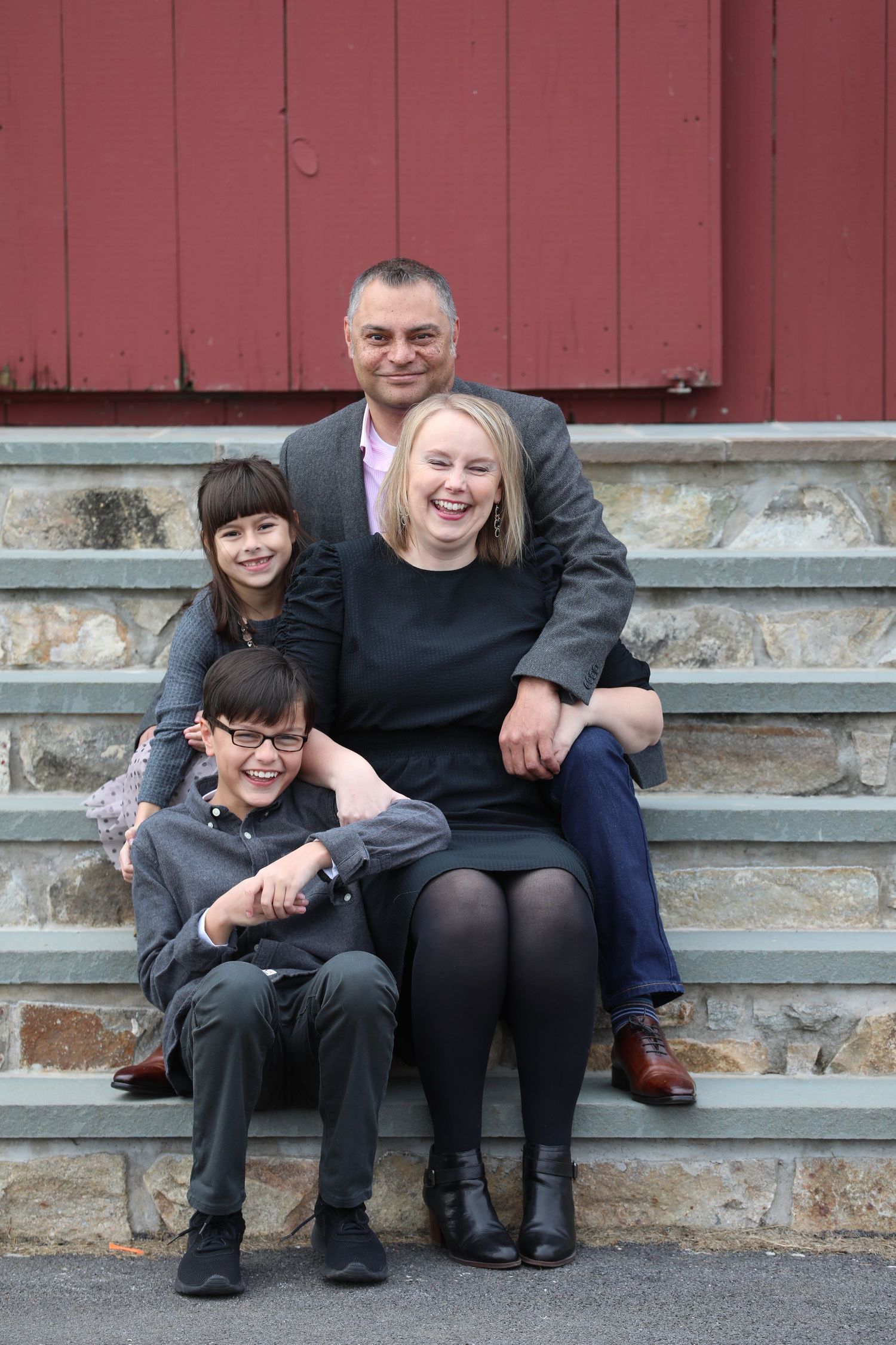 A cheerful group sits together on stone steps against a rustic red wall background.